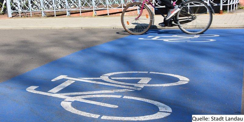 Straße mit Person, die Fahrrad fährt und einer weißen Fahrradmarkierung auf blauem Grund auf dem Boden.
